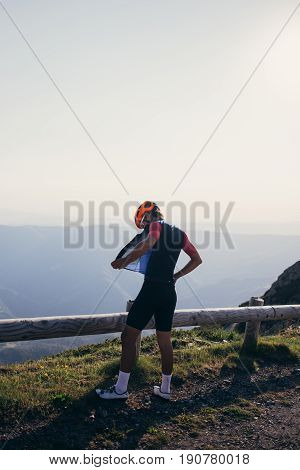 Vertical photo of road cyclist athlete standing on top of mountain summit after hard training and wears protective wind proof cycling vest