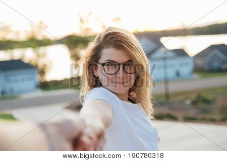 POV shot of a hand holding young attractive female girl in round glasses and white simple tshirt dancing in front of brand new house concept couple love happiness calm