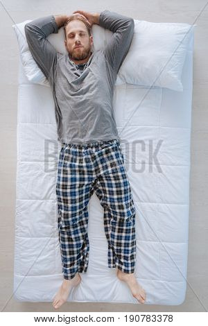 Being asleep. Pleasant nice bearded man lying on the bed and having dreams while being asleep