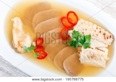 Homemade jelly chicken decorated with greens and eggs on plate on wooden background close up. Cold Meat Dishes