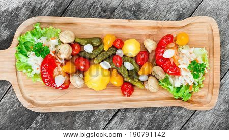 Assorted pickled vegetables - Sauerkraut cabbage peppers cucumbers tomatoes onions mushrooms and herbs on cutting board on wooden background close up. Snacks and Wine appetizers set. Top view