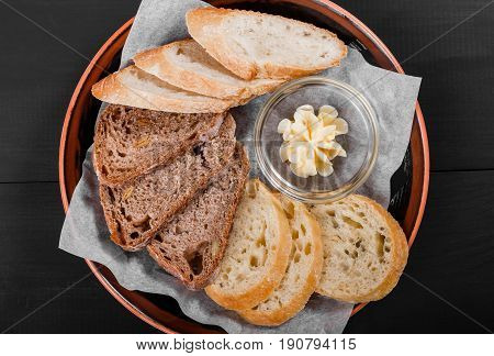 Top view of sliced wholegrain bread ciabatta and rye spikelets bread with butter on black wooden background. Bakery products. Hot and healthy breakfast top view flat lay