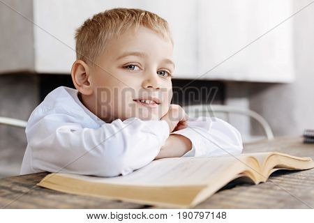 Bright child. Talented diligent brilliant kid taking a moment for resting while reading an old book and sitting at the table