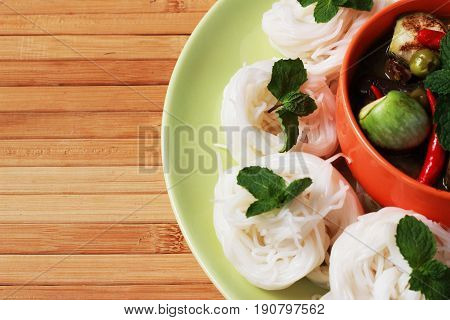 Green curry in an orange cup in the middle of a plate Thai-rice-flour Noodles (kanom jeen)