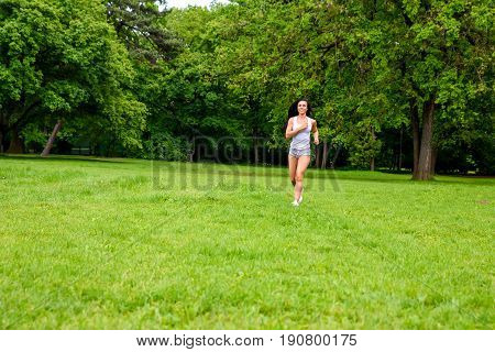 A beautiful young sporty girl running on a field in a park while wearing shorts and a top