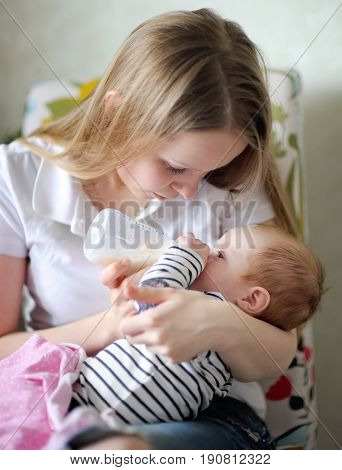 Adorable baby drinking milk from bottle in mother hands