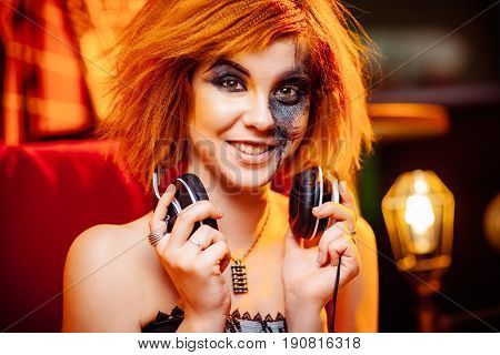 Redhaired girl in headphones with unusual makeup at the disco