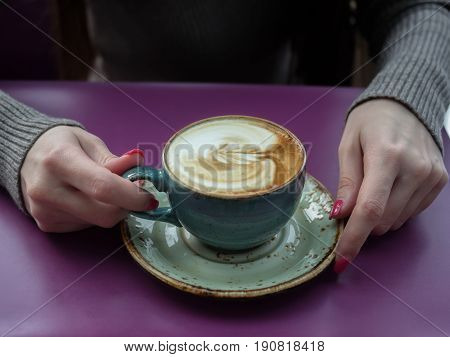 girl is holding a cup of coffee in her hands on a purple table.