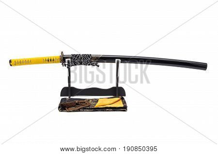 Japanese sword with yellow leather cord wrapped on handle and scabbard with ray skin on stand white background black silk bag at front.