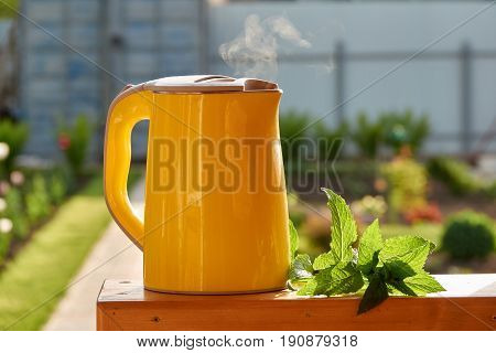 Tea with mint. Boiling yellow electric kettle in the garden.