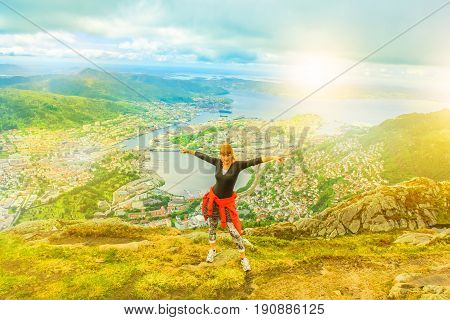 Happy traveler enjoying after hiking on Mount Ulriken at sunset. Norwegian tourism highlight. Bergen city skyline. Kiker woman in North Europe. Scenic norwegian landscape. Popular overlook landmark.