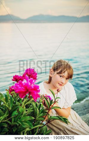 Outdoor portrait of adorable little girl posing with bright pink peonies by lake Geneva Switzerland