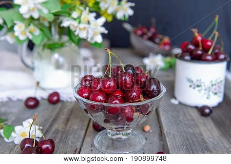 Fresh Cherry Fruit In Glass Vase, Other Dishes With Berries And Jar With Jasmine And Wildflowers On