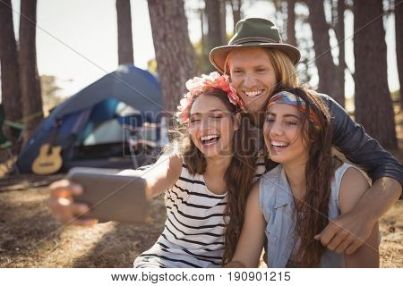 Happy friends clicking selfie while camping in forest on sunny day
