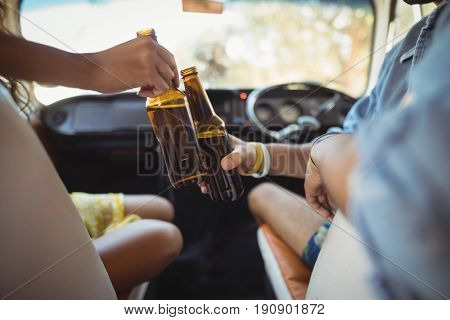 Midsection of friends toasting beer while sitting in van