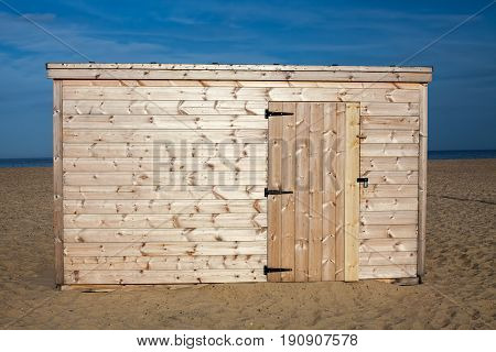 Unpainted beach hut. New wooden shed in the sunshine on the sand. Bare pine wood panelling on this new build cabin.