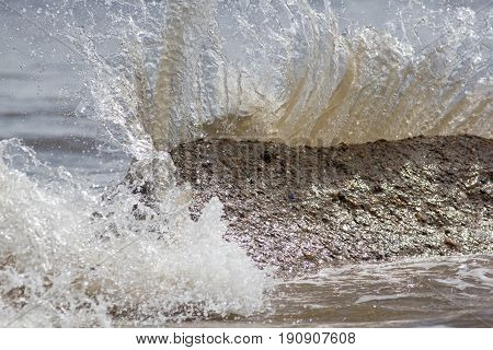 Force of nature. Splashing wave energy. Splash as sea water hits concrete rock. Fast shutter speed freezes water splashing. Image connotations of natural energy and coastal erosion.