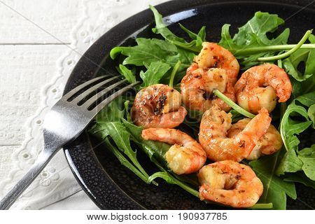 fried prawns or shrimps on arugula rocket salad with lemon and bread served on a black plate white tablecloth close up with selected focus narrow depth of field