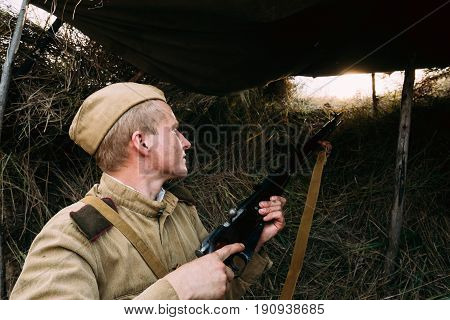 Dyatlovichi, Belarus - October 1, 2016: Reenactor Dressed As Russian Soviet Red Army Soldier Of World War II Hidden Sitting And Aiming Rifle Weapon From Trench, Hovel, Ambush In Autumn Meadow