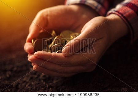 Farmer with handful of coins over soil land making money and gaining profit in agriculture
