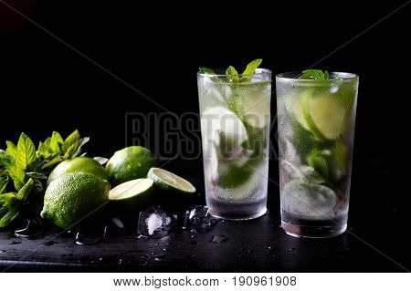 Mojito traditional summer vacation refreshing cocktail alcohol drink in glass, bar preparation soda water beverage, lime juice, mint leaves, sugar, and rum. Dark black background with copy space text