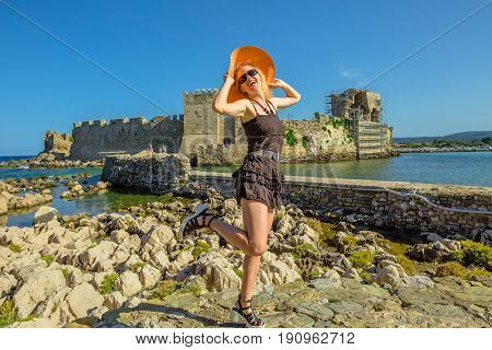 Happy attractive tourist vacation woman with sun hat enjoying on islet of Bourtzi. Methoni Venetian Castle, a medieval fortification, Peloponnese, Greece. Happiness travel holidays lifestyle concept