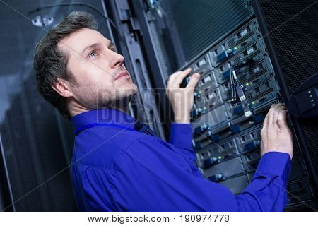 Cyber technology. Smart confident handsome man standing in front of the data server and doing his work while being a professional engineer