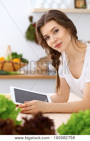 Young woman looking for a new recipe for cooking in a kitchen. Housewife is making online shopping by tablet computer and credit card.