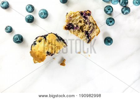 An overhead photo of two halves of a blueberry muffin with fresh blueberries and crumbs scattered around, with a place for text