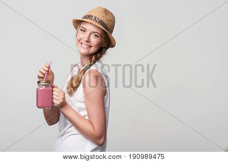 Smiling girl holding jar tumbler mug with pink smoothie drink, portrait over grey background with blank copy space