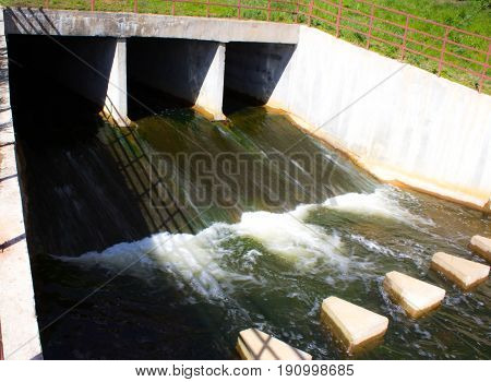Blue sky partially filled with fluffy white clouds, water falling over dam structures in the foreground.