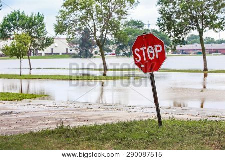 A stop sign at the edge of stormwater filling a flooded street 