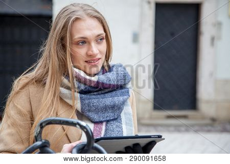 Blonde Beautiful Woman Holding Tablet On City Street. Portrait Of Young Woman Wearing Tartan Scarf S