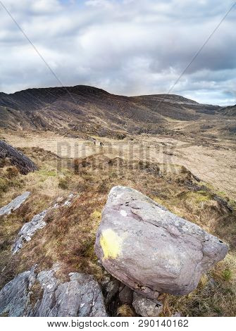Big Stone With Sign And Three People Hiking In Mountins In Gleninchaquin Park. Kenmare, County Kerry