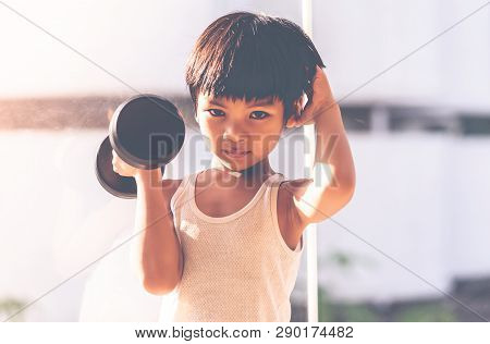 Little Boy Is Working Out With Dumbbell By The Windows City.