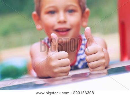 Happy Little Boy In A Straped T-shirt Shows The Ok Gesture At The Playground.