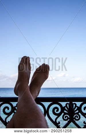 Legs on handrail with ocen and blue sky