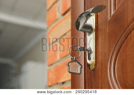 Key With House-shaped Trinket In Door Lock, Closeup. Space For Text
