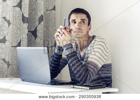 Portrait Of Young Man In Casual Wear On The Job Working On Laptop Looking At With Thoughtful Face