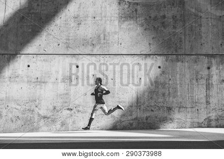 Muscular Man Athlete Sprinter Running Fast, Exercising Outdoors, Jogging Outside Against Gray Concre