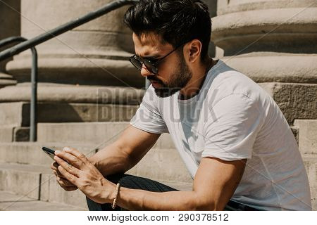 Handsome Bearded Hispanic Man Using Mobile Smartphone For Surfing Web Internet, Making Call And Look