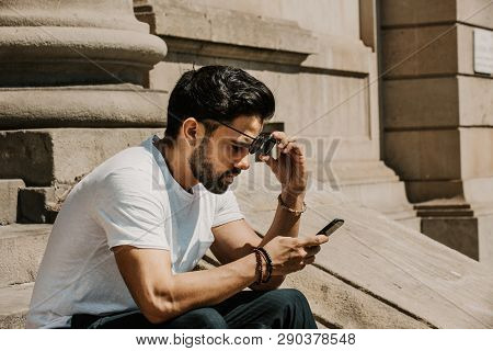 Handsome Bearded Hispanic Man Using Mobile Smartphone For Surfing Web Internet, Making Call And Look