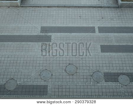 View From Top On Sidewalk Pavement Made Of Concrete Tiles With Lot Of Round Hatchways