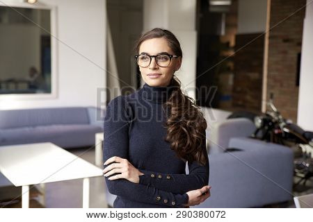 Attractive Young Woman Looking Thoughtfully And Smiling While Standing Indoor