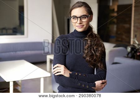 Attractive Young Woman Looking Thoughtfully And Smiling While Standing Indoor