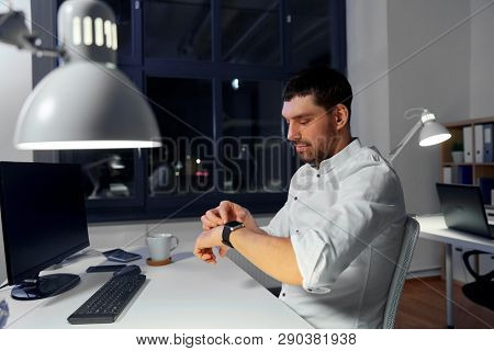 business, technology and time management concept - businessman using smart watch at nigh office