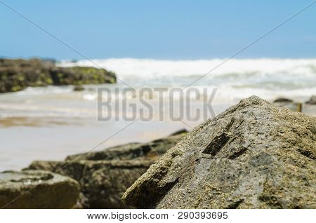 Stone On The Edge Of The Beach In The Foreground, In The Background The Waves Of The Sea