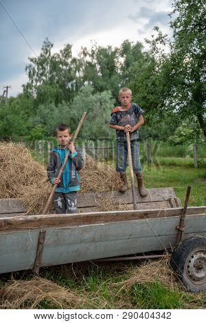 Litynia Village, Ukraine - June 02, 2018: Two Little Boys On Retro Cart. Work Near Hay For Livestock