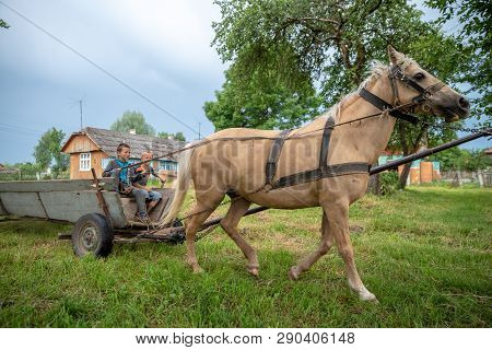 Litynia Village, Ukraine - June 02, 2018: Two Young Boys Riding On An Old Wooden Cart. Life In A Vil