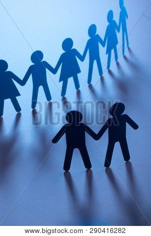 Black paper figure of male couple in front of a crowd of paper people holding hands on blue surface. Social movement, protest, minorities concept.
